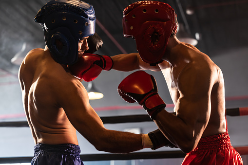 Two athletic and muscular body boxers with safety helmet or boxing head guard face off in fierce boxing match. Boxing fighter competitor fighting in the boxing ring. Impetus