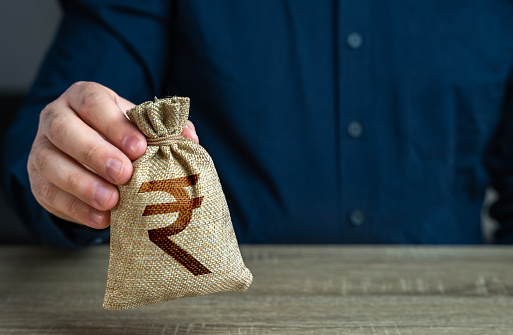 A man holds an indian rupee money bag. Deposits and savings. Loans and credits, mortgage. Economics and currency exchange, stock market. Banks and finance. Investments, fundraising. Funding and grants