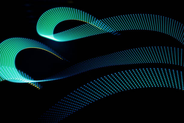 istock Blue turquoise glowing neon curved wave of light as curls with dotted stripes on black background, pattern. Abstract background with motion light effect in hipster style. 1979563172