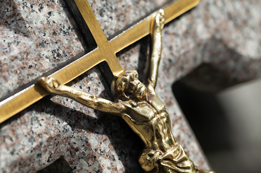Jesus crucified golden metal statue. Weathered granite cross. Graveyard background. Shiny gold symbol.