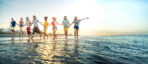 Crowd of friends running to sunset sea - Summer holidays concept with guys and girls enjoying beach sunrise - Happy young people with arms up standing on coastline - Colorful background photo