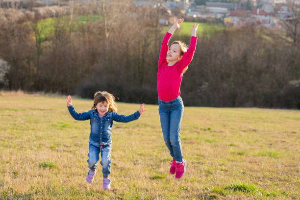 Two happy children with a bouquet of wildflowers running and jumping in a park. Time together.