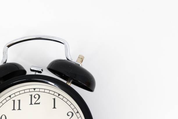 istock A black alarm clock with two bells on top, chrome handle, and legs, set against a white background. Timeless design meets functionality in this sleek, monochromatic timepiece. 1979613633