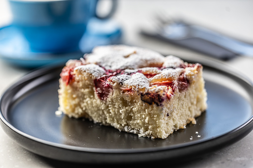 Fruity plum cake on a plate and next to a mug with coffee on a table in a cafe.