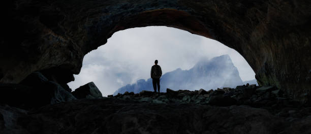 istock Adventurous Man Hiker standing in cave with dramatic cloud and snowy mountain view. 1979623050