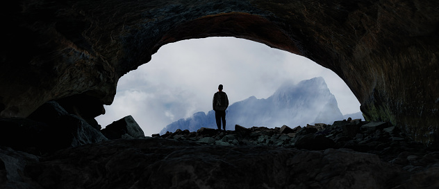 Adventurous Man Hiker standing in cave with dramatic cloud and snowy mountain view. Adventure Composite. 3d Rendering Peak. Dramatic night scene.