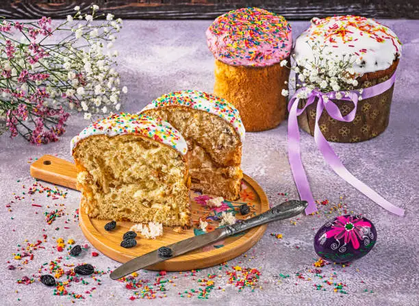 A cut Eastercake on a tray is a traditional Ukrainian holiday baking. Knife, raisins, Easter eggs, sprinkles as decoration. Festive composition.