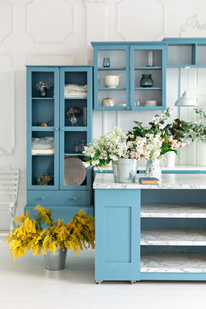 istock Summer kitchen with decor. Cozy home decor. Kitchen island in dining room. Kitchen utensil, dishes and plate on shelves. Blue kitchen interior with furniture. Stylish cuisine with flowers in vase 1979663227