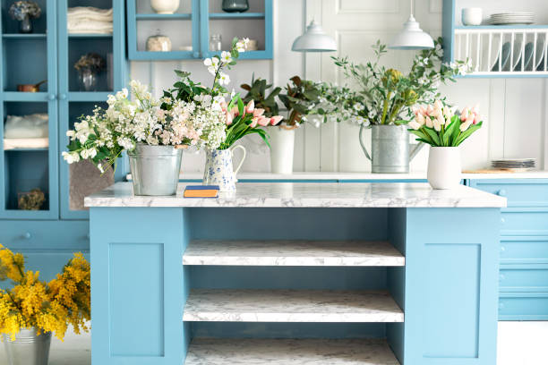 istock Summer kitchen with decor. Cozy home decor. Kitchen island in dining room. Kitchen utensil, dishes and plate on shelves. Blue kitchen interior with furniture. Stylish cuisine with flowers in vase 1979663760