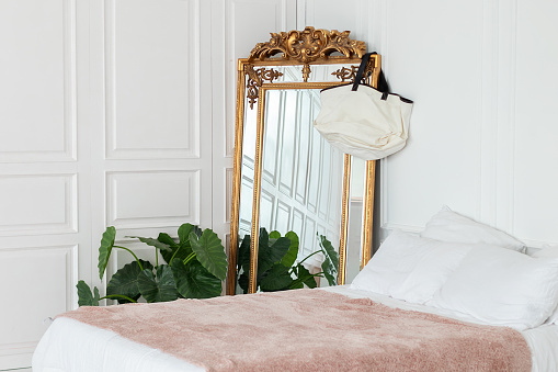 Gold vintage mirror on a white wall background. Interior white bedroom with comfortable bed with plaid and large mirror, copy space. Elegant mirror with beautiful details. scandinavian decoration room