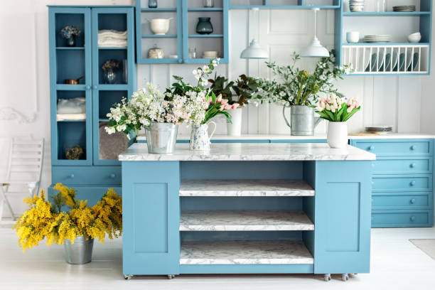 istock Summer kitchen with decor. Cozy home decor. Kitchen island in dining room. Kitchen utensil, dishes and plate on shelves. Blue kitchen interior with furniture. Stylish cuisine with flowers in vase 1979666926
