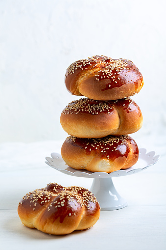 Stack of sweet round mini challah bread with sesame seeds in a vintage metal stand on a light background.Concept of festive baking.