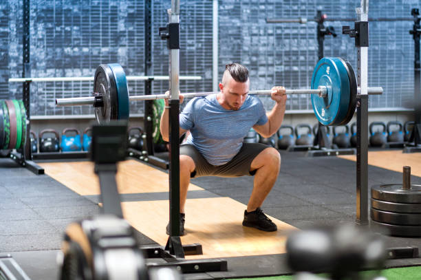 istock Man doing exercises with barbell on back while squatting in gym 1979740441