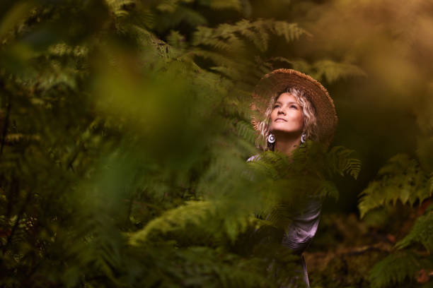 Young woman with straw hat day dreaming among greenery in the forest.