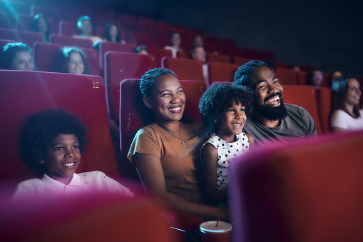 Happy African American family enjoying while watching a movie in cinema.