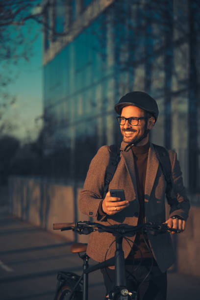 istock A cheerful businessman holding a mobile phone and pushing a bicycle. 1979765930