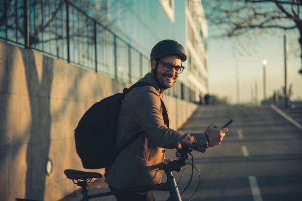 istock A portrait of a happy businessman with a backpack using a smartphone and leaning on handlebars of a bicycle 1979766981