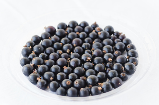 Black berries on white. Blackcurrants in a transparent bowl isolated on a white background. Blackcurrant with copy space closeup. Currant organic berries harvest - healthy eating and food concept