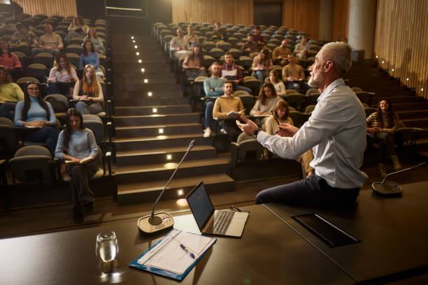 Mature professor talking on a class at lecture hall. Senior professor talking in front of large group of his students during a lecture in amphitheater. middle age adult studying stock pictures, royalty-free photos & images