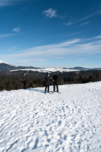 A married couple is skiing in the mountains. A man and a woman skiers are posing against the backdrop of snow-capped mountains. The concept of skiing