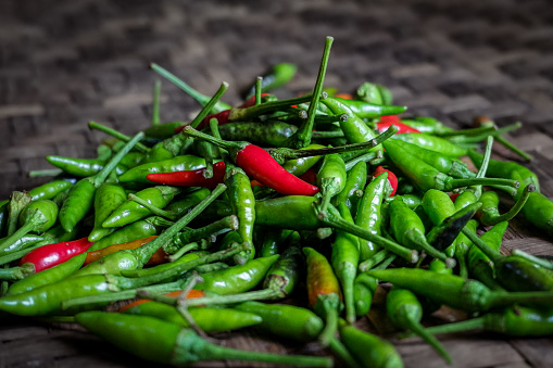 a pile of fresh chili peppers on a woven bamboo tray, red and green chili peppers