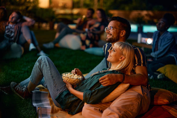 istock Young couple eating popcorn while watching a movie at night in the backyard. 1979814964
