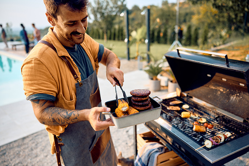 Happy man preparing food on barbecue grill in the backyard.