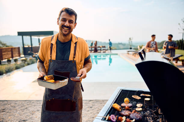 istock Happy man preparing barbecue during poolside party with friends and looking at camera. 1979818207