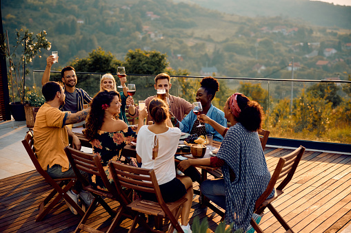 Group of happy diverse friends having fun while toasting at dining table on a patio. Copy space.