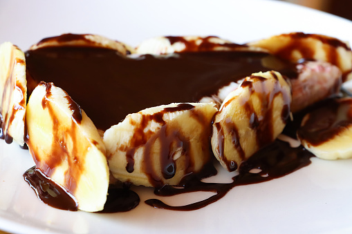 Stock photo showing close-up view of a restaurant dessert of Banoffee Pie on a white plate covered in chocolate sauce.