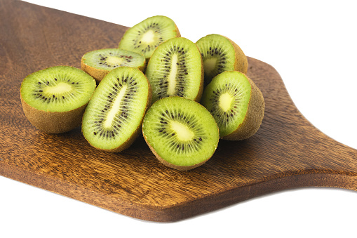 A healthy ripe kiwi cut in half lies on a wooden cutting board, isolated on a white background.