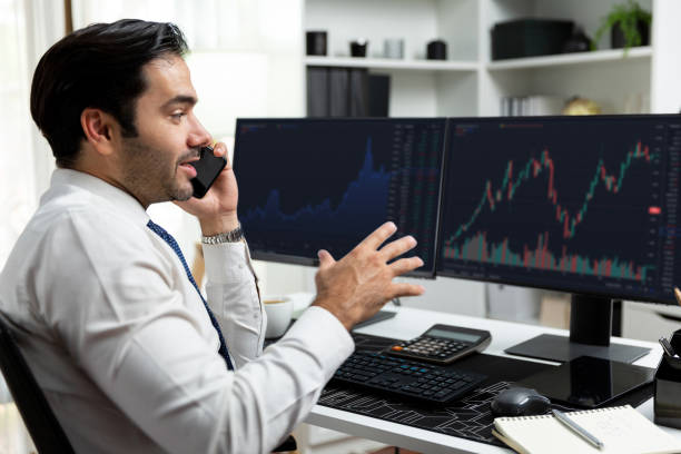istock Trader calling to consultant or partner with two stock exchange screen. Surmise. 1979871538