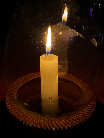 Stock photo showing close-up, nighttime view of a candle flame in a glass hurricane lamp on an al fresco restaurant table in the dark.