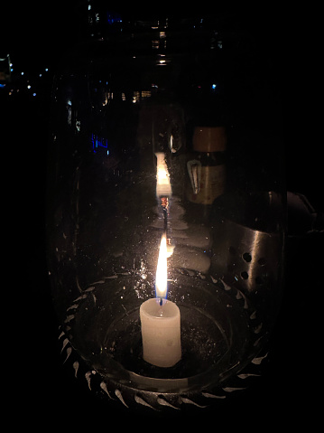 Stock photo showing close-up, nighttime view of a candle flame in a glass hurricane lamp on an al fresco restaurant table in the dark.
