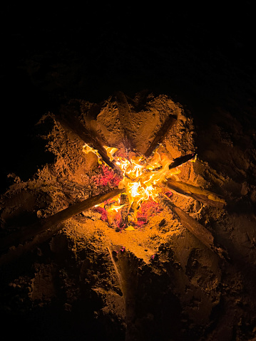 Stock photo showing close-up, elevated, night-time view of flames in beach fire pit which has been lit in preparation of a beach party.