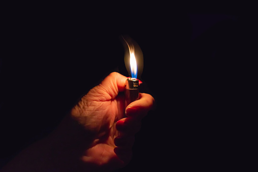 Woman hand holding a burning lighter in the dark black background.Closeup,selective focus.Copy space.