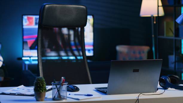 istock Dimly lit apartment with office desk in front of smart TV displaying news program 1979901952