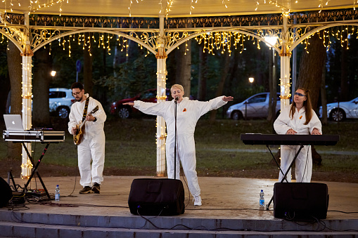 Svetlogorsk, Russia - 13.08.2023 - Local pop rock music band performs in gazebo of city public park, energetic outdoor performance of keyboardist, guitarist and vocalist in evening lights of park