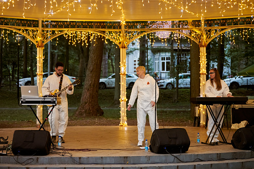 Svetlogorsk, Russia - 13.08.2023 - Local pop rock music band performs in gazebo of city public park, energetic outdoor performance of keyboardist, guitarist and vocalist in evening lights of park