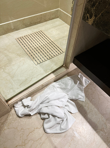 Stock photo showing close-up, elevated view of a wet towel left on tiled floor of luxury bathroom with glass shower cubicle.