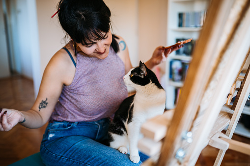 Portrait of a beautiful female artist painting in her studio with a cat in her lap