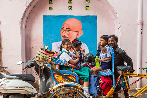 School children riding in cycle-rickshaw with Gandhi mural in the background December 3 2013, Chennai, (Madras), India