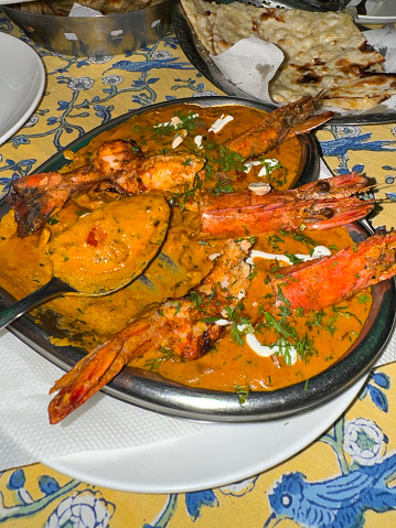 Stock photo showing close-up, elevated view of heart-shaped serving dish of king prawn curry with a serving spoon.