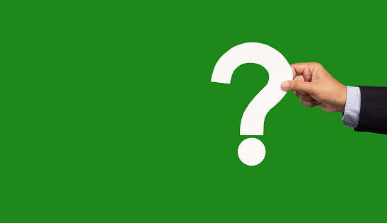 Question mark symbol. Hand holding a white question mark symbol against a green background. Close-up photo. Space for text