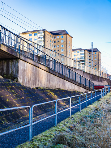 This image captures apartment buildings towering above a sloped pedestrian walkway basking in the sunlight of a clear day.