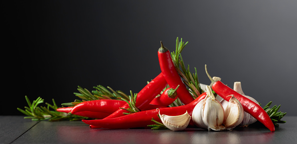 Red hot chili peppers, garlic, and rosemary on a black background.Copy space.