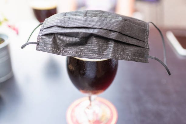 glass of beer,black face mask on a beer glass beer on a table. coronavirus restrictions considering drinking in pubs. - 5412 stock-fotos und bilder