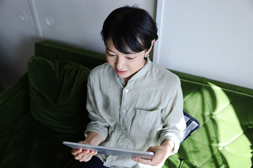 Middle-aged Asian woman with serious expression.
Woman who is cancer patient using a digital tablet.
Women with cancer are finding out about cancer and feeling scared. Woman Searching for treatment on the internet.  
Telemedicine.