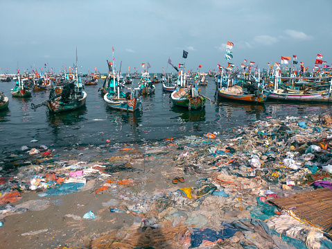 portrait of fishing boats leaning on a beach in the village of Weru Paciran Lamongan in dirty conditions full of plastic waste scattered around. beach trash