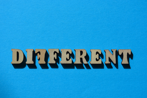 Different, with a backward F, word in wooden alphabet letters isolated on blue background with copy space